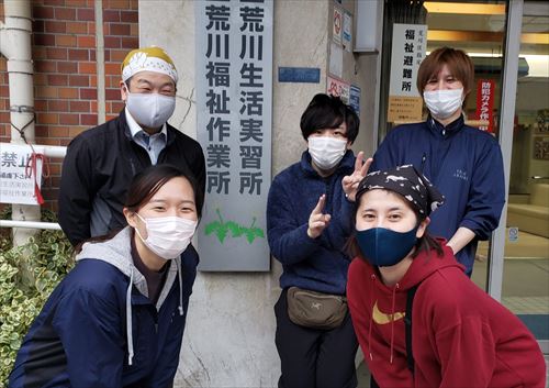 荒川生活実習所、荒川福祉作業所の看板前で笑顔な職員さんたちの様子